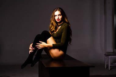 Güzel dansçı. Kız model. Kız bir şapkanın içinde oturuyor ve masaya oturuyor. Güzel iç çamaşırlı bir kız. Kız masada oturuyor ve maskaralık yapıyor, surat asıyor. pürüzsüz, bakımlı bacaklar.