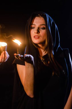 Gizemli genç kız siyah pelerin giyiyor, cadıların Şenlik ateşinin yanındaki ormanda Şabat günü