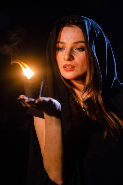 Gizemli genç kız siyah pelerin giyiyor, cadıların Şenlik ateşinin yanındaki ormanda Şabat günü