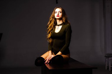 Güzel dansçı. Kız model. Kız bir şapkanın içinde oturuyor ve masaya oturuyor. Güzel iç çamaşırlı bir kız. Kız masada oturuyor ve maskaralık yapıyor, surat asıyor. pürüzsüz, bakımlı bacaklar.