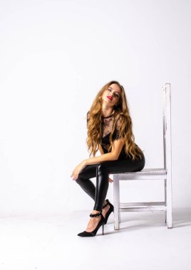 deri kıyafet giyen siyah saçlı kız tam uzunlukta portre. bir silah tutarken oturmuş poz, beyaz bir stüdyo arka plan üzerinde izole.