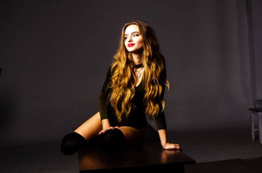 Güzel dansçı. Kız model. Kız bir şapkanın içinde oturuyor ve masaya oturuyor. Güzel iç çamaşırlı bir kız. Kız masada oturuyor ve maskaralık yapıyor, surat asıyor. pürüzsüz, bakımlı bacaklar.