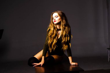 Güzel dansçı. Kız model. Kız bir şapkanın içinde oturuyor ve masaya oturuyor. Güzel iç çamaşırlı bir kız. Kız masada oturuyor ve maskaralık yapıyor, surat asıyor. pürüzsüz, bakımlı bacaklar.