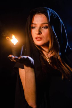 Gizemli genç kız siyah pelerin giyiyor, cadıların Şenlik ateşinin yanındaki ormanda Şabat günü