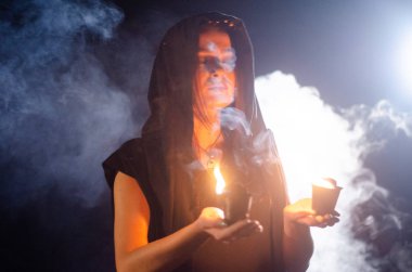 Gizemli genç kız siyah pelerin giyiyor, cadıların Şenlik ateşinin yanındaki ormanda Şabat günü