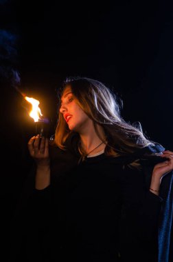 Gizemli genç kız siyah pelerin giyiyor, cadıların Şenlik ateşinin yanındaki ormanda Şabat günü