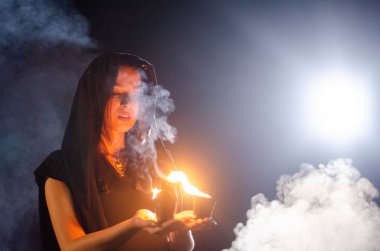 Gizemli genç kız siyah pelerin giyiyor, cadıların Şenlik ateşinin yanındaki ormanda Şabat günü