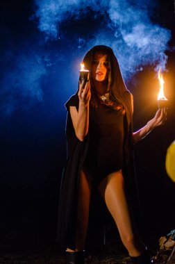 Gizemli genç kız siyah pelerin giyiyor, cadıların Şenlik ateşinin yanındaki ormanda Şabat günü
