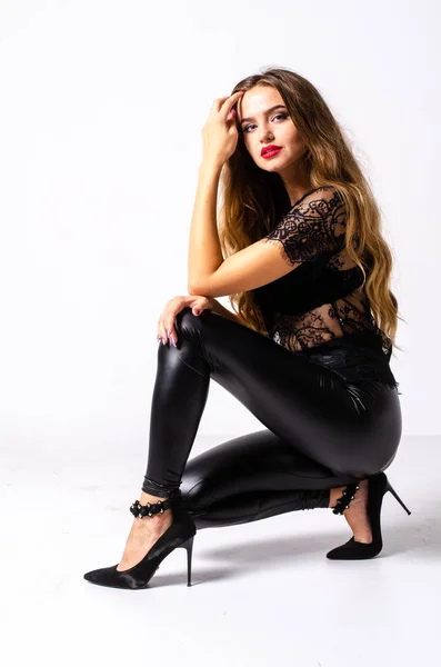 Full length portrait of black haired girl wearing leather outfit. seated pose while holding a gun, isolated on a white studio background. — Stock Photo, Image