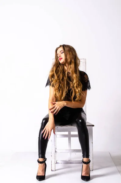 Teljes hosszúságú portréja Fekete hajú lány visel bőr ruhában. ülő pózol, miközben egy pisztolyt, izolált egy fehér stúdió háttér. — Stock Fotó