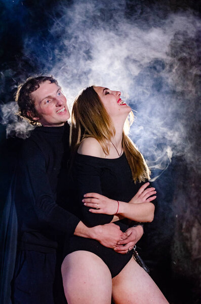 young sexy woman in a black bodysuit with a man posing against a background of smoke