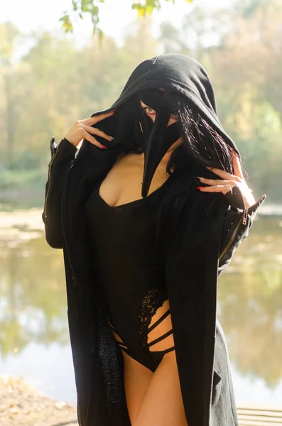 黒いカーニバルの衣装を着た美しい若い女性と森の上にポーズをとる仮面 — ストック写真