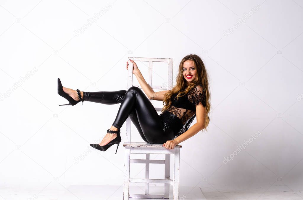 full length portrait of black haired girl wearing leather outfit. seated pose while holding a gun, isolated on a white studio background.