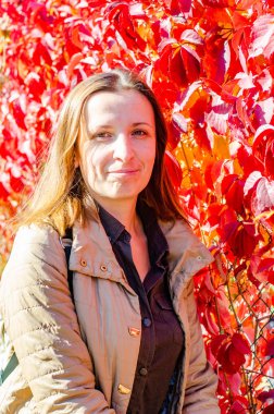 Parkta kırmızı bir sarmaşık duvarın yanında duran kadının portresi.