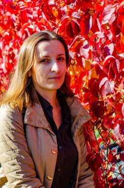 Parkta kırmızı bir sarmaşık duvarın yanında duran kadının portresi.