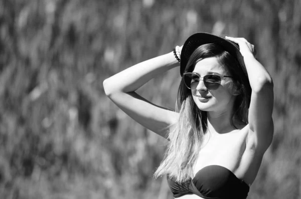 Girl in a hat and glasses in a swimsuit posing on the beach — Stock Photo, Image