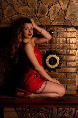 Bir sandalyede oturan bir uzun kırmızı Abiye çok güzel seksi kadın dekoratif şömine yakın. Güzel yeni yıl ve Noel sahne, güzellik moda Model portre.