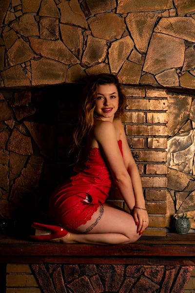 자에 앉아 긴 빨간 이브닝 드레스에 화려한 섹시 한 여성 장식 화재 장소 근처. 아름 다운 새 해와 크리스마스 장면, 뷰티 패션 모델 초상화. — 스톡 사진