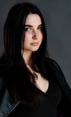 Karanlık stüdyoda şık giyinmiş esmer bir kadın poz veriyor.  