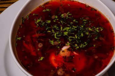 Çorba, ekşi kremalı borç, arka planda boncuk ve turşu. Borç beyaz bir tabakta, ekmek dilimleri ahşap bir kesme tahtasında, turşular ahşap bir tabakta..