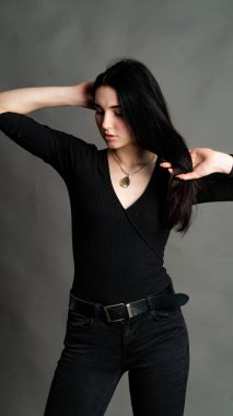 Yüksek tahta koltukta bacak bacak üstüne atmış esmer bir kadının portresi. Geniş paçalı pantolon giyen şık bir kız. Gri arkaplanda stüdyo çekimi