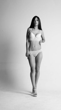 Beyaz iç çamaşırlı ve yüksek topuklu bir kız beyaz arka planda poz veriyor.. 