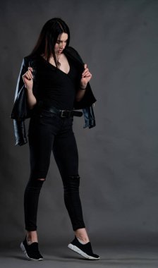 Karanlık stüdyoda şık giyinmiş esmer bir kadın poz veriyor.  