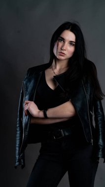 Karanlık stüdyoda şık giyinmiş esmer bir kadın poz veriyor.  