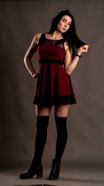 Karanlık stüdyoda şık giyinmiş esmer bir kadın poz veriyor.  