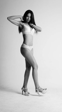 Beyaz iç çamaşırlı ve yüksek topuklu bir kız beyaz arka planda poz veriyor.. 