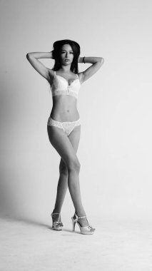 Beyaz iç çamaşırlı ve yüksek topuklu bir kız beyaz arka planda poz veriyor.. 