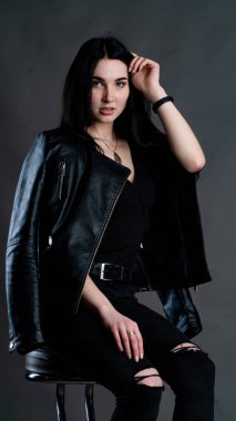 Karanlık stüdyoda şık giyinmiş esmer bir kadın poz veriyor.  