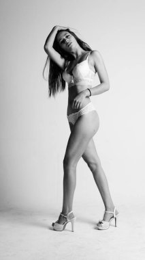 Beyaz iç çamaşırlı ve yüksek topuklu bir kız beyaz arka planda poz veriyor.. 