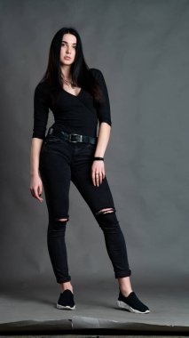 Yüksek tahta koltukta bacak bacak üstüne atmış esmer bir kadının portresi. Geniş paçalı pantolon giyen şık bir kız. Gri arkaplanda stüdyo çekimi