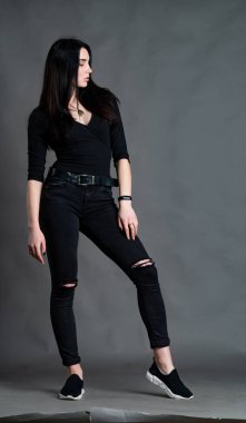 Yüksek tahta koltukta bacak bacak üstüne atmış esmer bir kadının portresi. Geniş paçalı pantolon giyen şık bir kız. Gri arkaplanda stüdyo çekimi