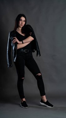 Karanlık stüdyoda şık giyinmiş esmer bir kadın poz veriyor.  