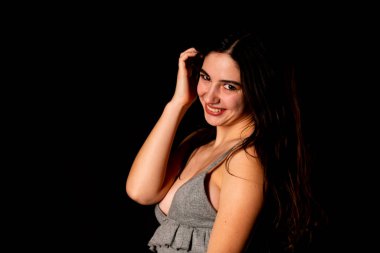 Koyu kahverengi saçlı, gri elbiseli, esmer, güzel bir kadın. Stüdyo arka planında poz veriyor.  