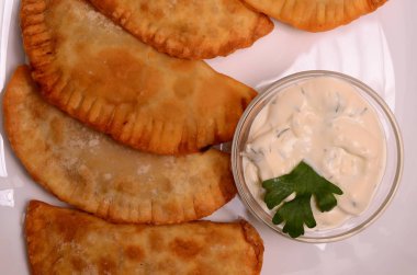 Özbek Doğu Tatar mutfağı, et ve suluguni ile cheburek peynirli sebze ve Yeşiller ahşap bir masa üzerinde beyaz bir tabak içinde.