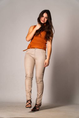 Güzel esmer manken şık kıyafetler içinde, aydınlık odada poz veriyor. 