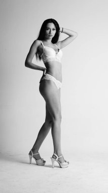 Beyaz iç çamaşırlı ve yüksek topuklu bir kız beyaz arka planda poz veriyor.. 