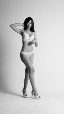 Beyaz iç çamaşırlı ve yüksek topuklu bir kız beyaz arka planda poz veriyor.. 