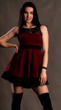 Koyu renk saçlı, kırmızı elbiseli, karanlık stüdyoda poz veren genç ve seksi bir kadın..