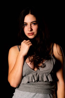 Koyu kahverengi saçlı, gri elbiseli, esmer, güzel bir kadın. Stüdyo arka planında poz veriyor.  