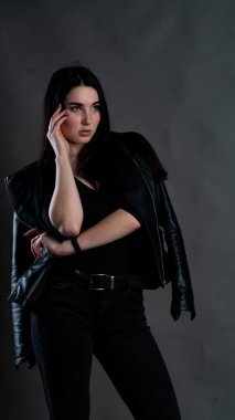 Karanlık stüdyoda şık giyinmiş esmer bir kadın poz veriyor.  