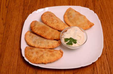 Özbek Doğu Tatar mutfağı, et ve suluguni ile cheburek peynirli sebze ve Yeşiller ahşap bir masa üzerinde beyaz bir tabak içinde.