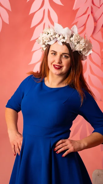 attractive woman in blue dress and floral wreath posing at studio