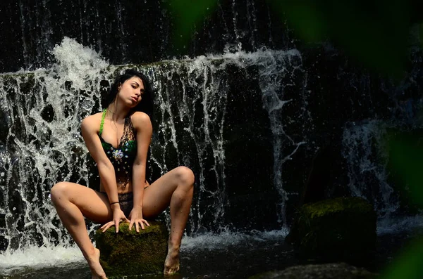 Young brunette model posing against a waterfall