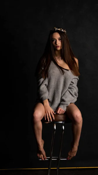 Vacker sexig tjej, poserar en kort grå klänning, svart bakgrund stol — Stockfoto