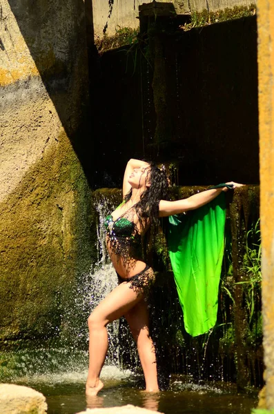 Young brunette model posing against a waterfall