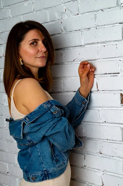 Menina morena em uma jaqueta verde e sutiã fica perto da parede de tijolo branco . — Fotografia de Stock